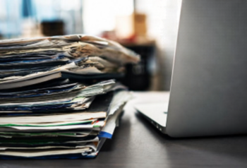 A pile of papers next to a laptop