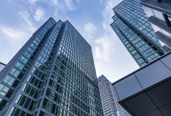 Tall glass office buildings viewed from below, representing enterprise organizations evaluating DAM solutions for brand consistency, approved asset access and scalable content management