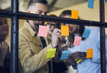 Business team reviewing a workflow diagram on a glass window, representing the duplication, version confusion and brand risk that can happen when enterprise teams manage assets in shared drives