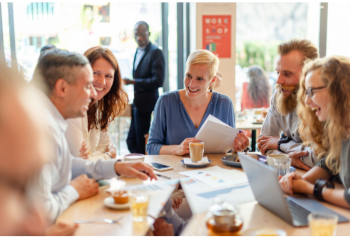 Foundation team meeting, discussing documents and smiling, seated around a table with laptops and coffee