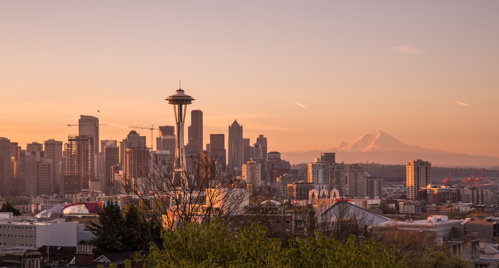 Seattle skyline at sunset featuring the Space Needle and Mount Rainier in the distance.