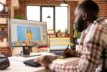 Designer editing digital marketing assets on a desktop monitor with additional files on a laptop