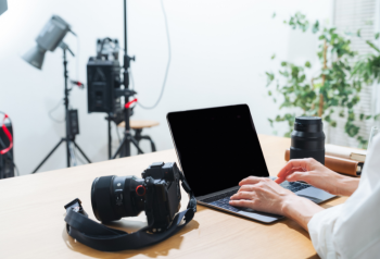 Photographer working on a laptop beside a camera and studio equipment