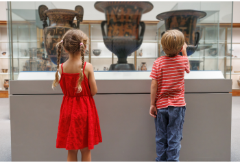 A young boy and girl standing by a museum case featuring antique pottery