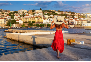 Traveler in a red dress walking along a waterfront toward a coastal town