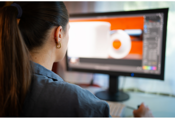 Designer working at a desk with creative tools and image libraries on screen, representing how digital asset management helps design teams manage approved assets, templates and Adobe workflows