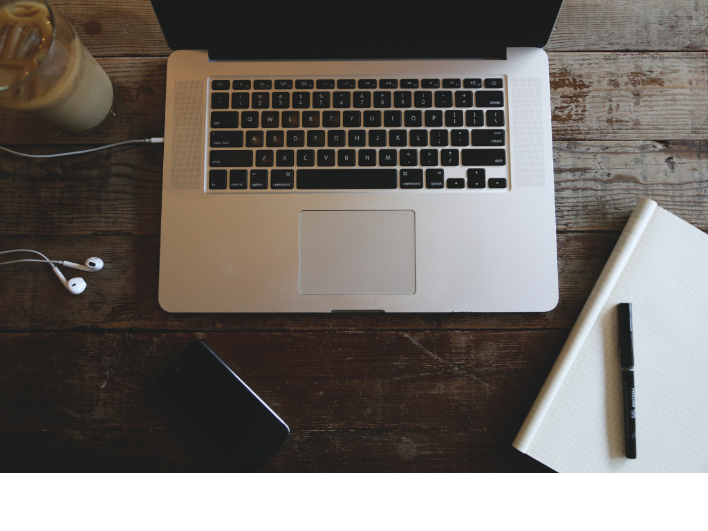 Overhead view of a laptop, smartphone, notebook, pen, and earbuds on a wooden desk.  Copy
