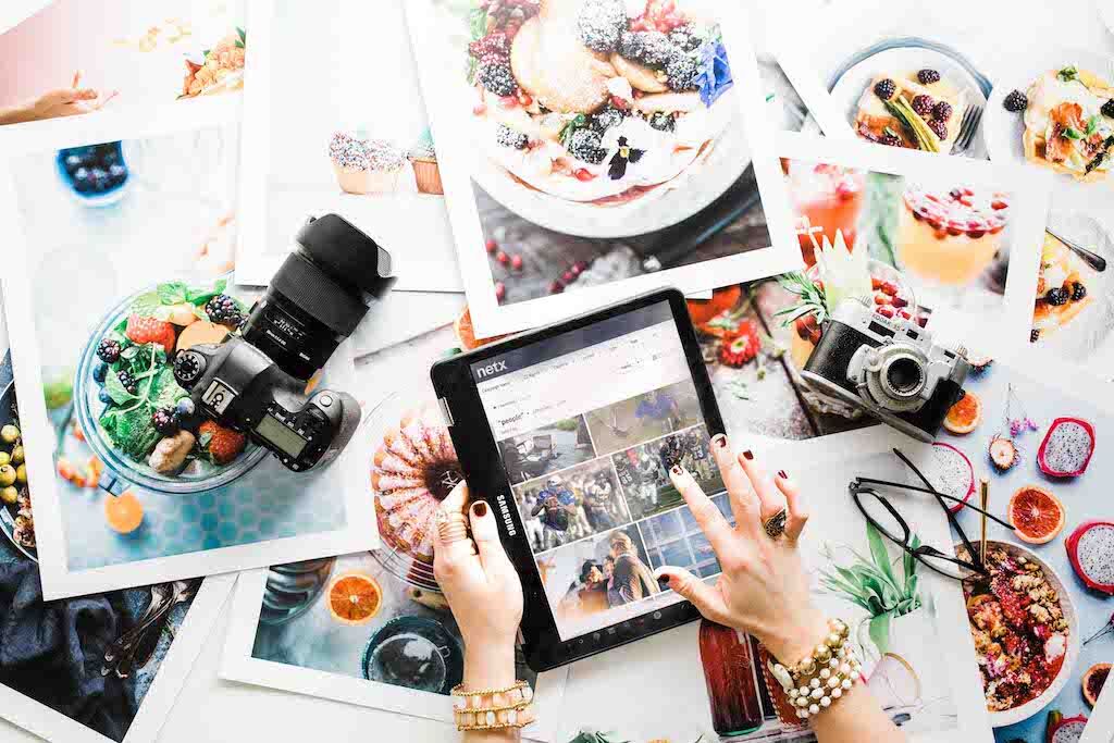 Overhead view of a creative workspace with cameras, printed photographs, and a tablet displaying the NetX digital asset management interface.