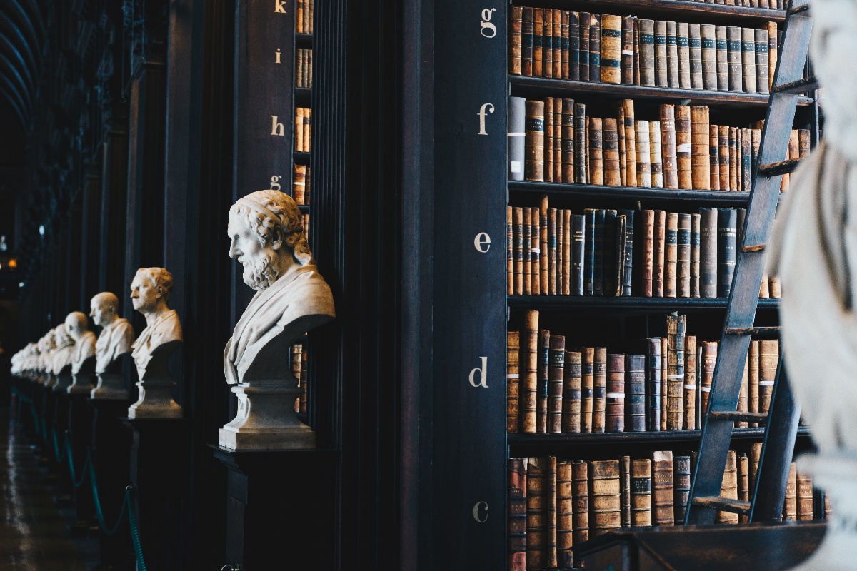 Historic library interior featuring marble busts, shelves of antique books, and a wooden ladder.