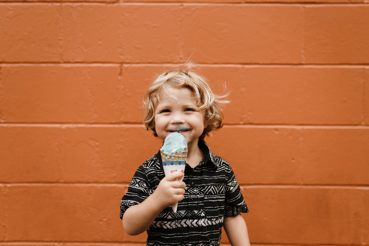 Smiling young child holding a blue ice cream cone against an orange wall.