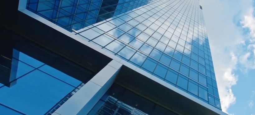 Glass corporate office building viewed from below, representing enterprise digital asset management for large organizations managing content across teams, brands and locations