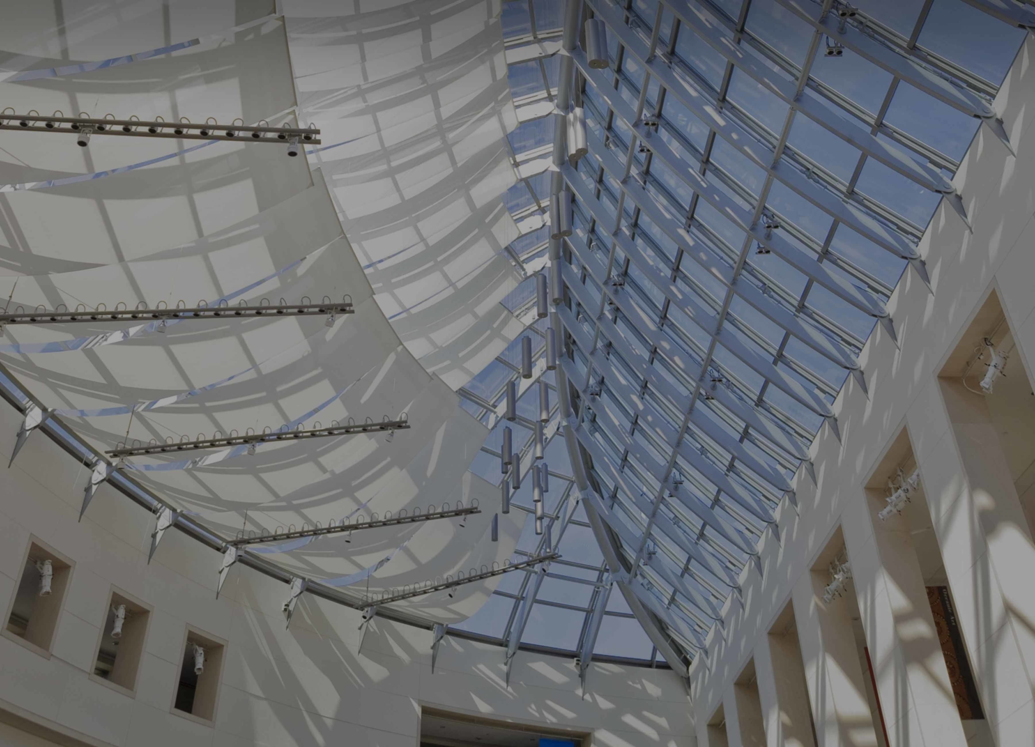  Interior view of the Peabody Essex Museum atrium featuring a curved glass ceiling, white structural beams, and natural light.