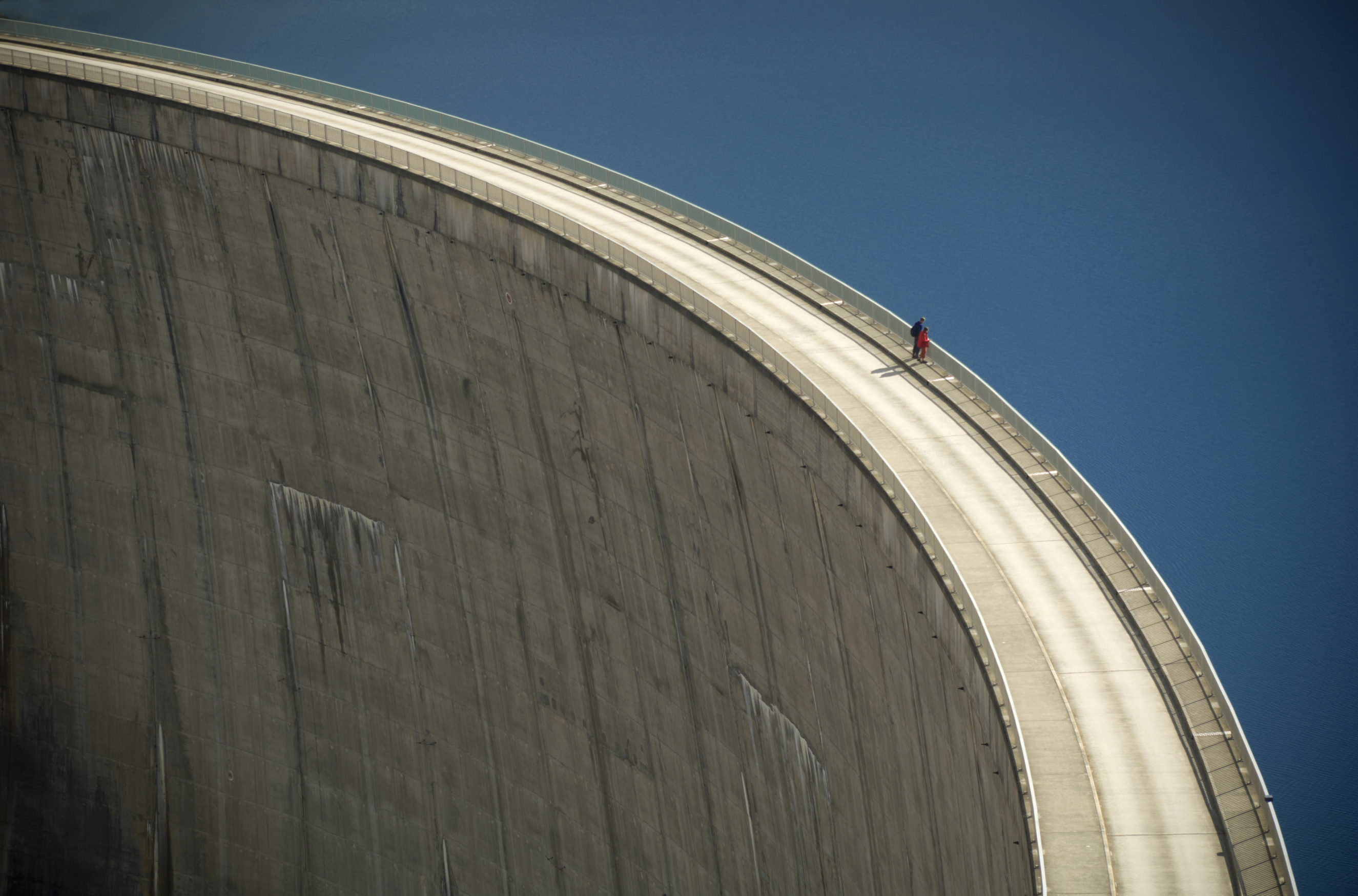 Person walking along the curved edge of a large concrete dam, illustrating a streamlined path to digital asset uploads.